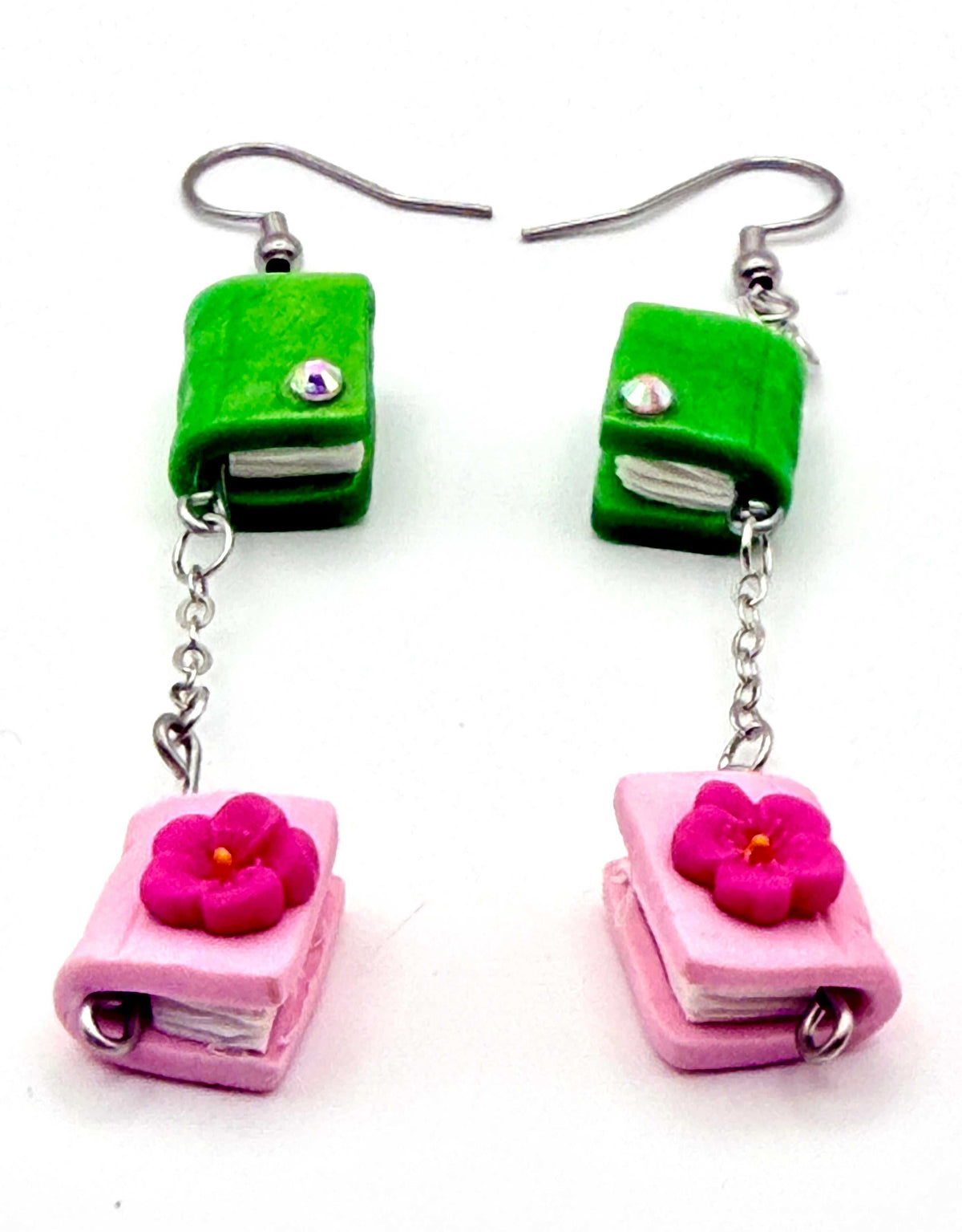 Close-up of pink and green book earrings, showcasing unique book design and adorned with tiny flowers and rhinestones.