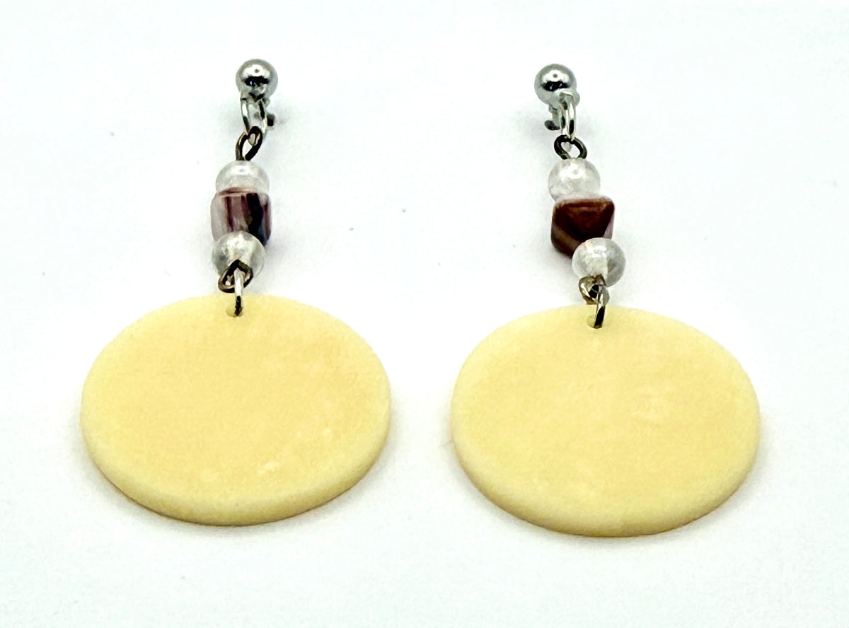 A pair of dangle earrings featuring large, flat, circular pale yellow discs hanging from silver-toned posts with small decorative beads, shown on a plain white background.