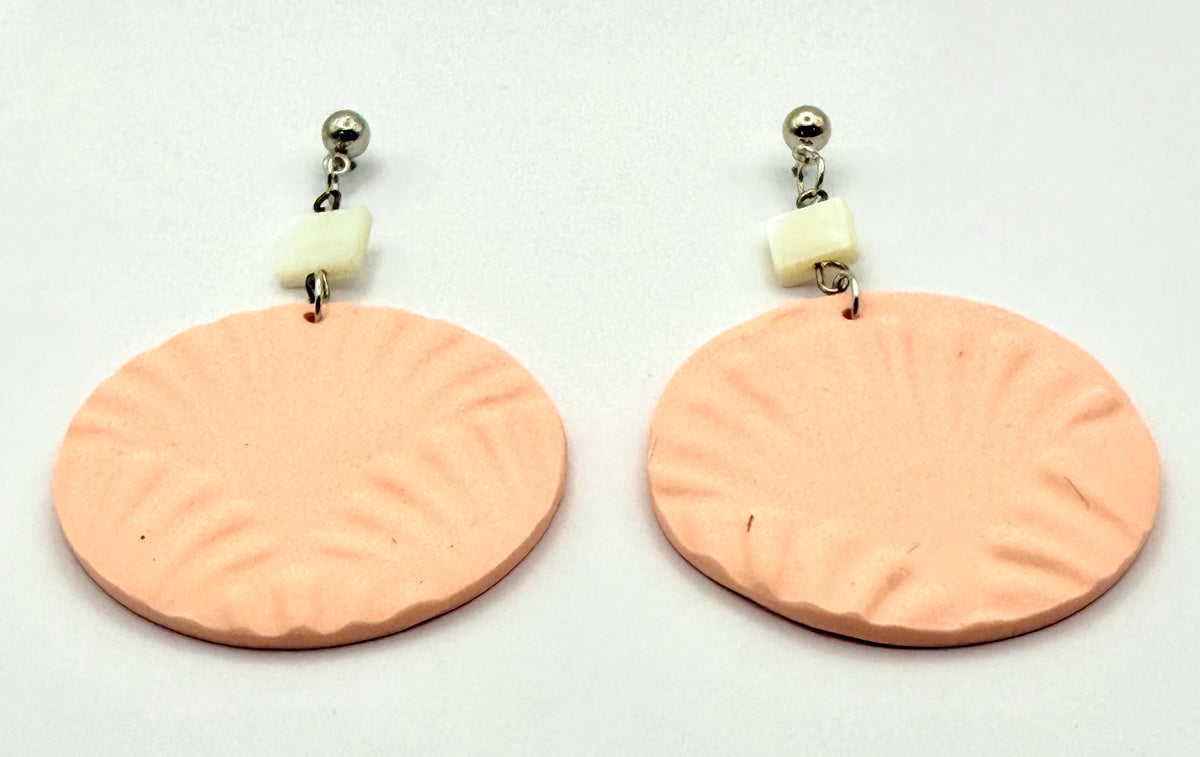 A pair of handmade dangle earrings featuring textured peach-pink circular disc charms with radial grooves, attached to small cream-colored beads and silver ball studs on a plain white background.