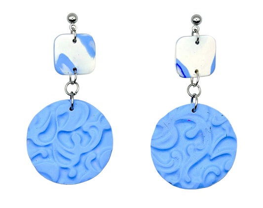 A pair of handmade drop earrings featuring textured light blue circular discs and white square charms with blue marbled details, suspended from silver-toned posts on a white background.