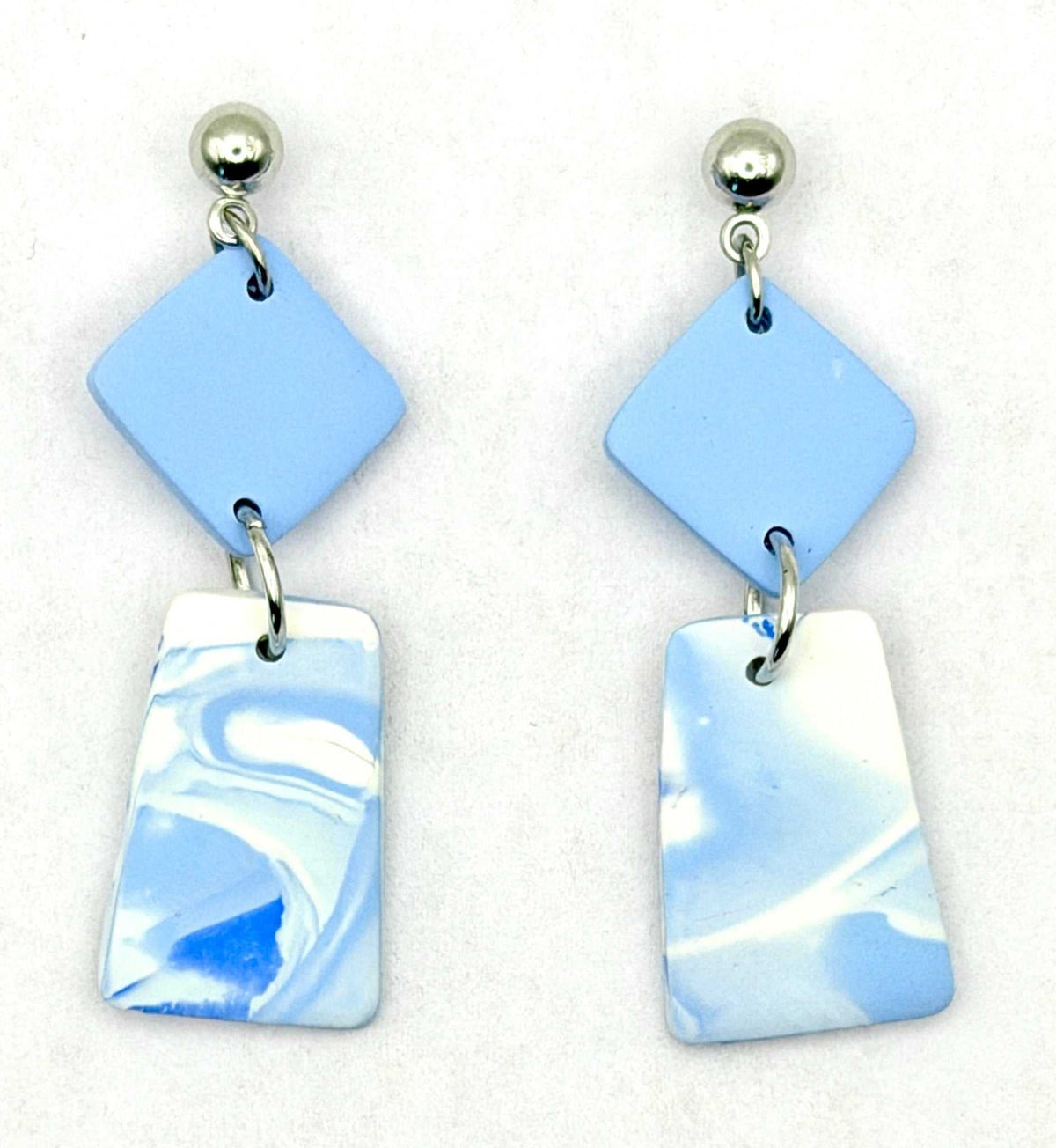 A pair of handmade dangle earrings featuring light blue and white marbled resin pieces with silver-tone ball studs, displayed on a clean white background.
