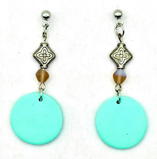 A pair of dangle earrings featuring large, flat turquoise blue-green circular discs hanging from silver-toned posts with ornate silver beads and a small brown faceted bead in the middle, set against a plain white background.