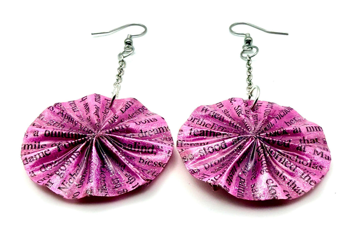 A pair of handmade dangle earrings featuring pink and purple book-paper disc charms with black printed text, suspended from silver fishhook wires on a white background.