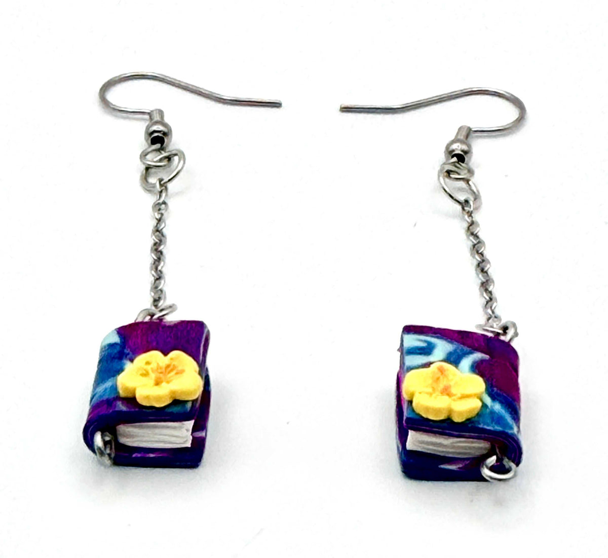 Close-up of purple swirled book earrings with chain links and silver hooks, showcasing unique swirled design and adorned with an accenting flower.