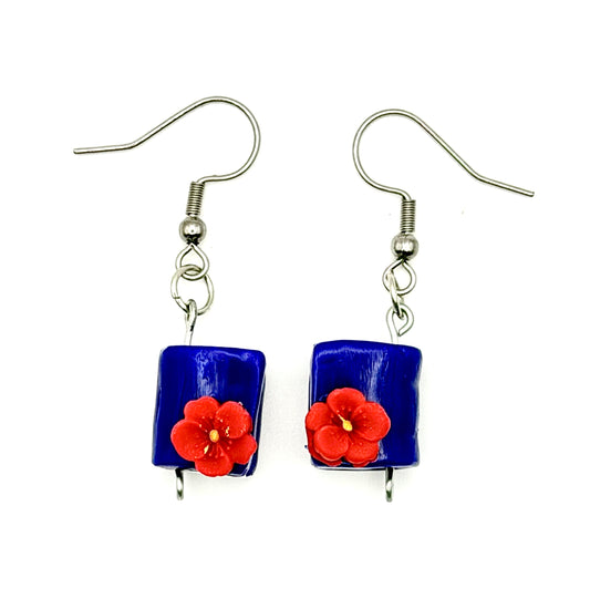 A pair of handmade drop earrings featuring rectangular cobalt blue polymer clay book pendants with a small red flower charm in the center, suspended from silver-tone French hook ear wires on a white background.