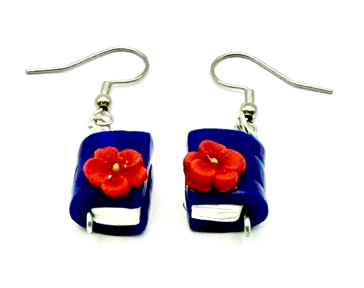 A pair of handmade dangle earrings shaped like blue books with red flowers on the front, suspended from silver-tone fishhook wires against a plain white background.
