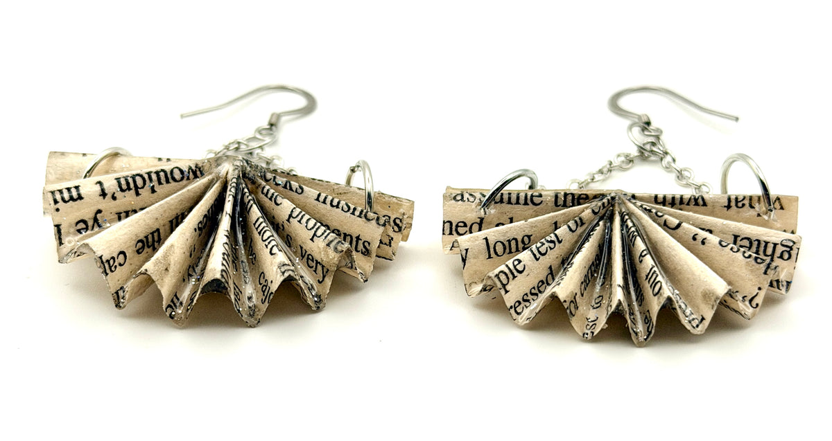 A pair of handmade dangle earrings made from folded pages of a book with black printed text on aged beige paper, suspended from silver fishhook wires, shown against a plain white background.