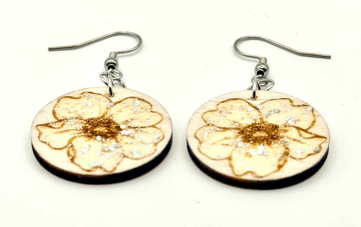 A pair of round wooden dangle earrings featuring a laser-engraved flower design with silver-tone fishhook wires, displayed on a clean white background.