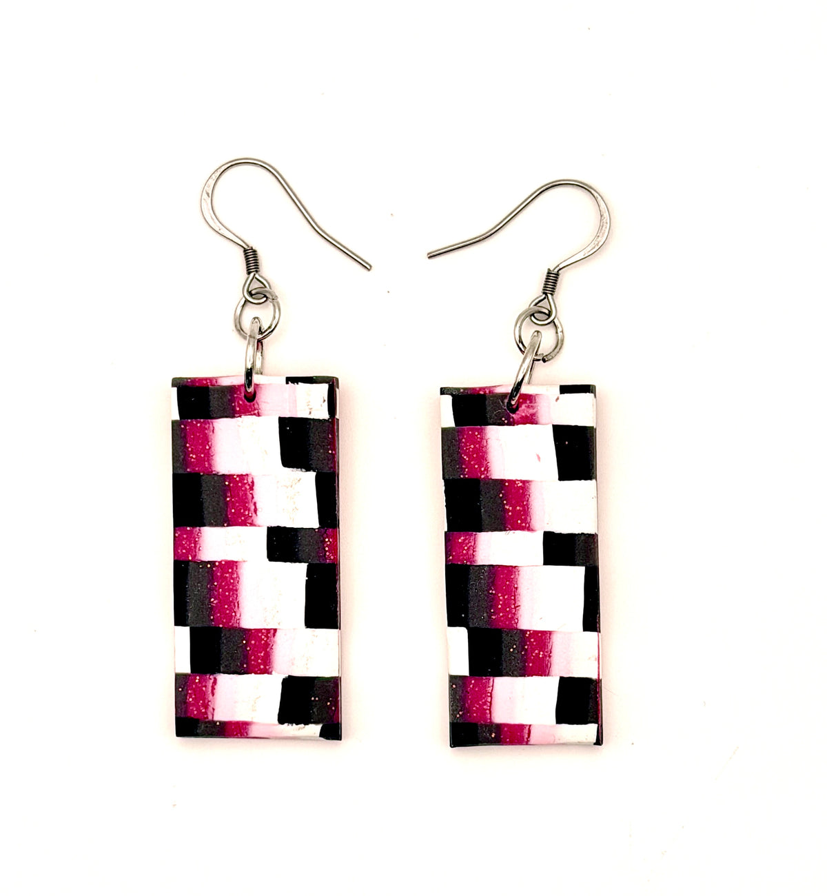 A pair of rectangular drop earrings with a black, white, and magenta geometric pattern, suspended from silver fishhook ear wires on a plain white background.