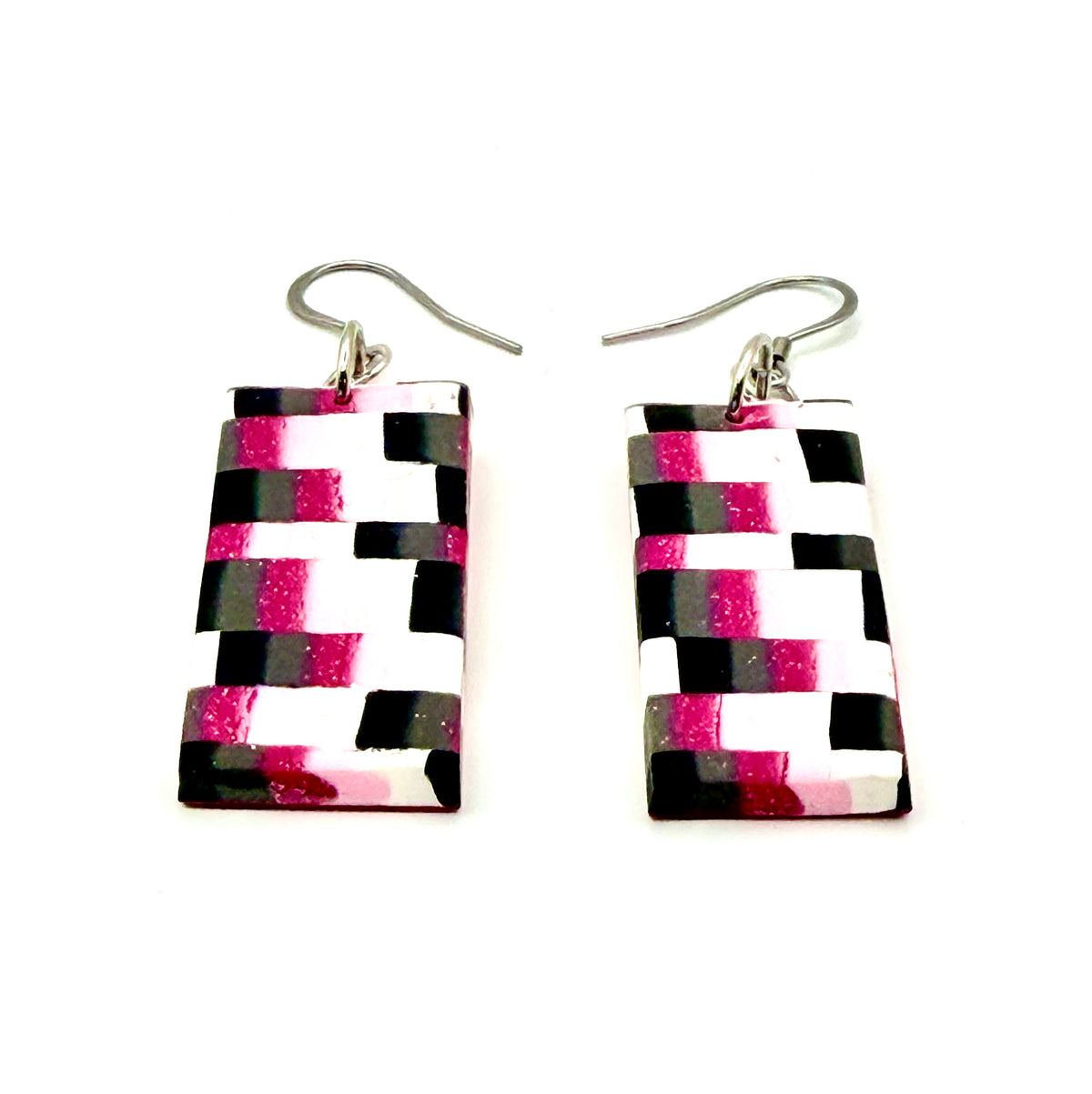A pair of rectangular drop earrings with a black, white, and hot pink geometric pattern, suspended from silver fishhook wires on a plain white background.