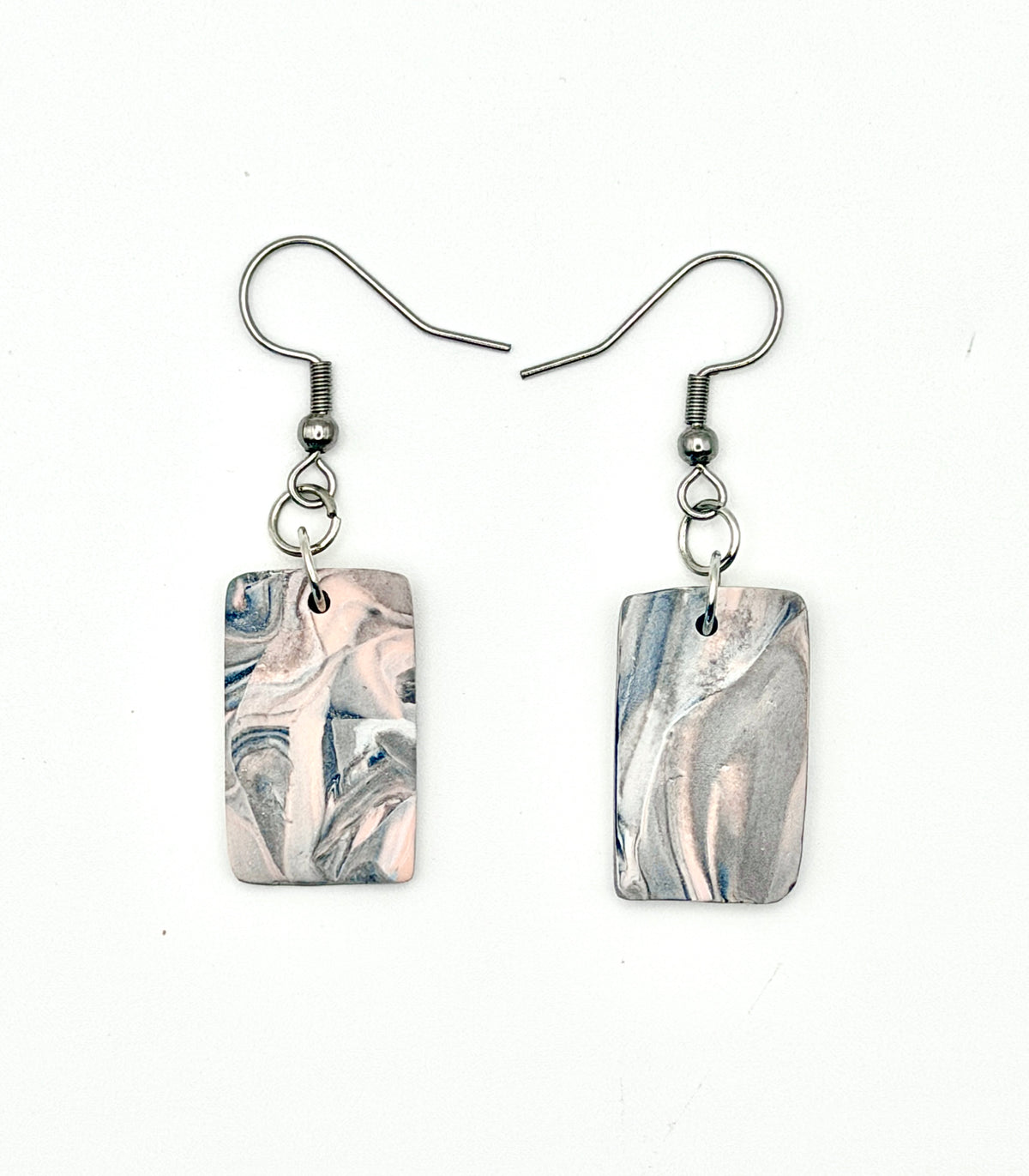 A pair of rectangular drop earrings with a light pink, gray, and white marble pattern, suspended from silver fishhook wires on a white background.