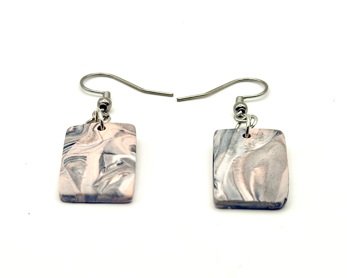 A pair of handmade square drop earrings featuring a marbled clay design in shades of gray, white, and soft pink, suspended from silver-tone French hook wires on a plain white background.