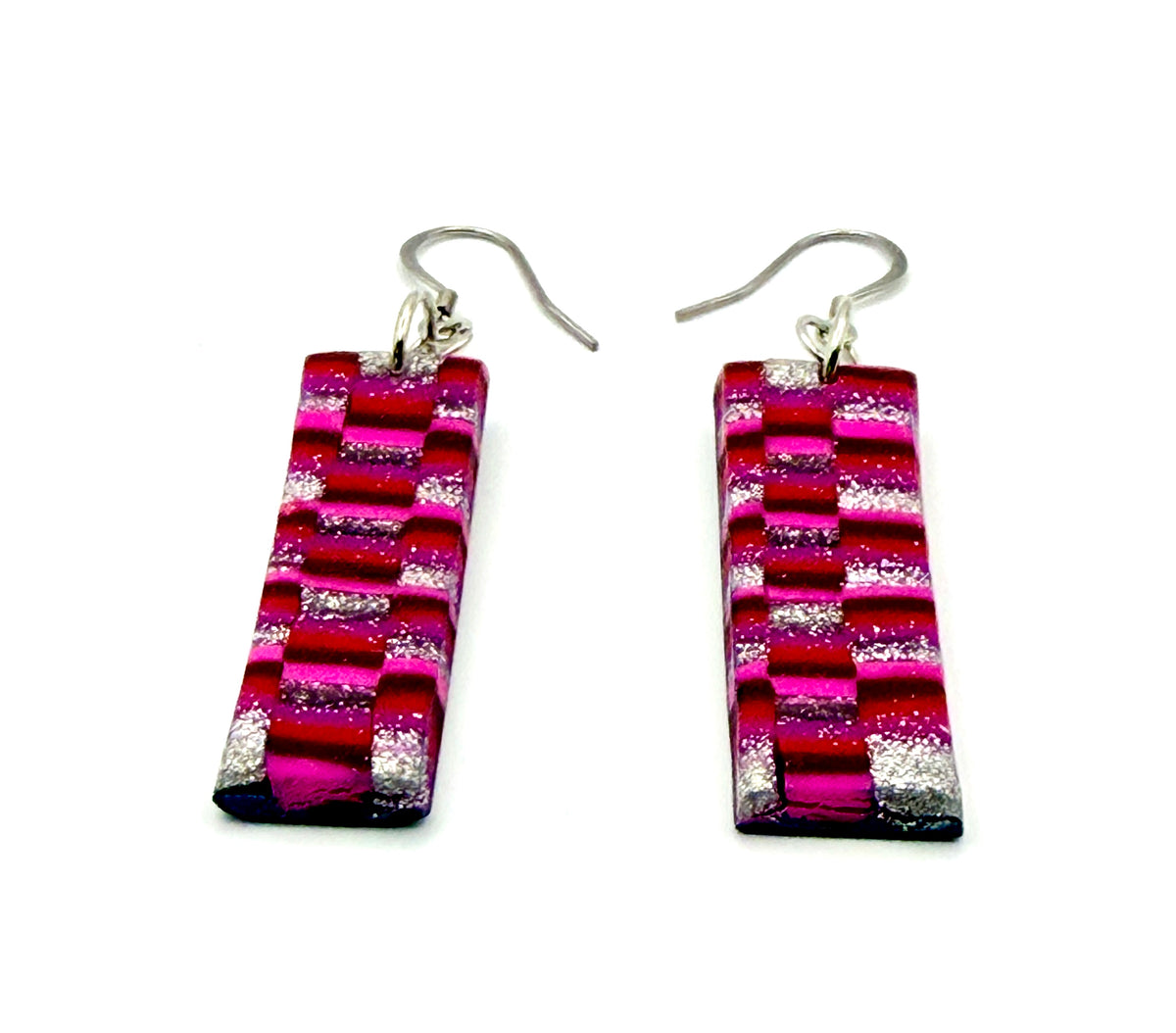 A pair of rectangular drop earrings made from textured, glittery strips in shades of magenta, pink, red, and silver, suspended from silver fishhook wires on a plain white background.