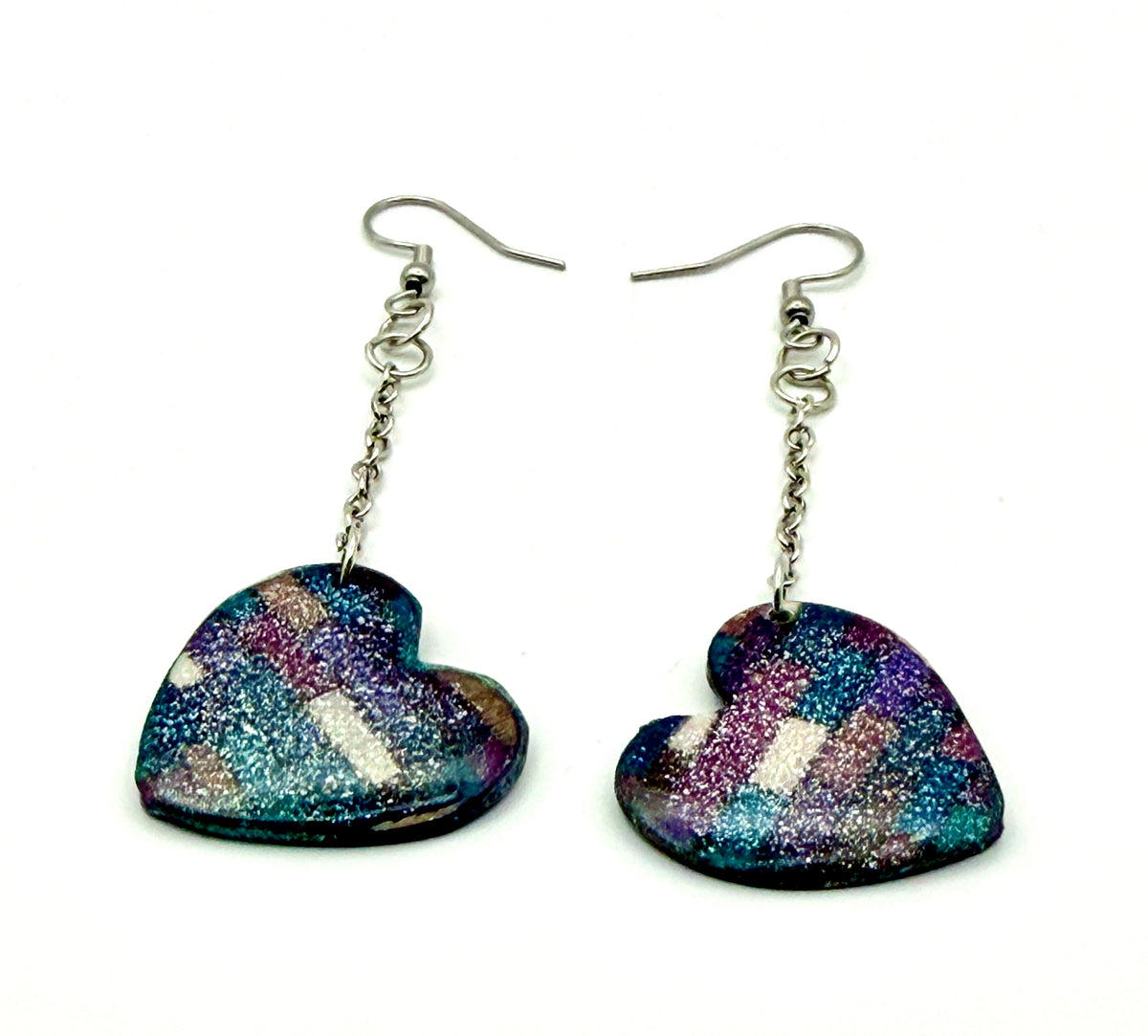 A pair of heart-shaped dangle earrings with a glittery finish showing shades of blue, purple, and pink, suspended from silver fishhook wires on a white background.