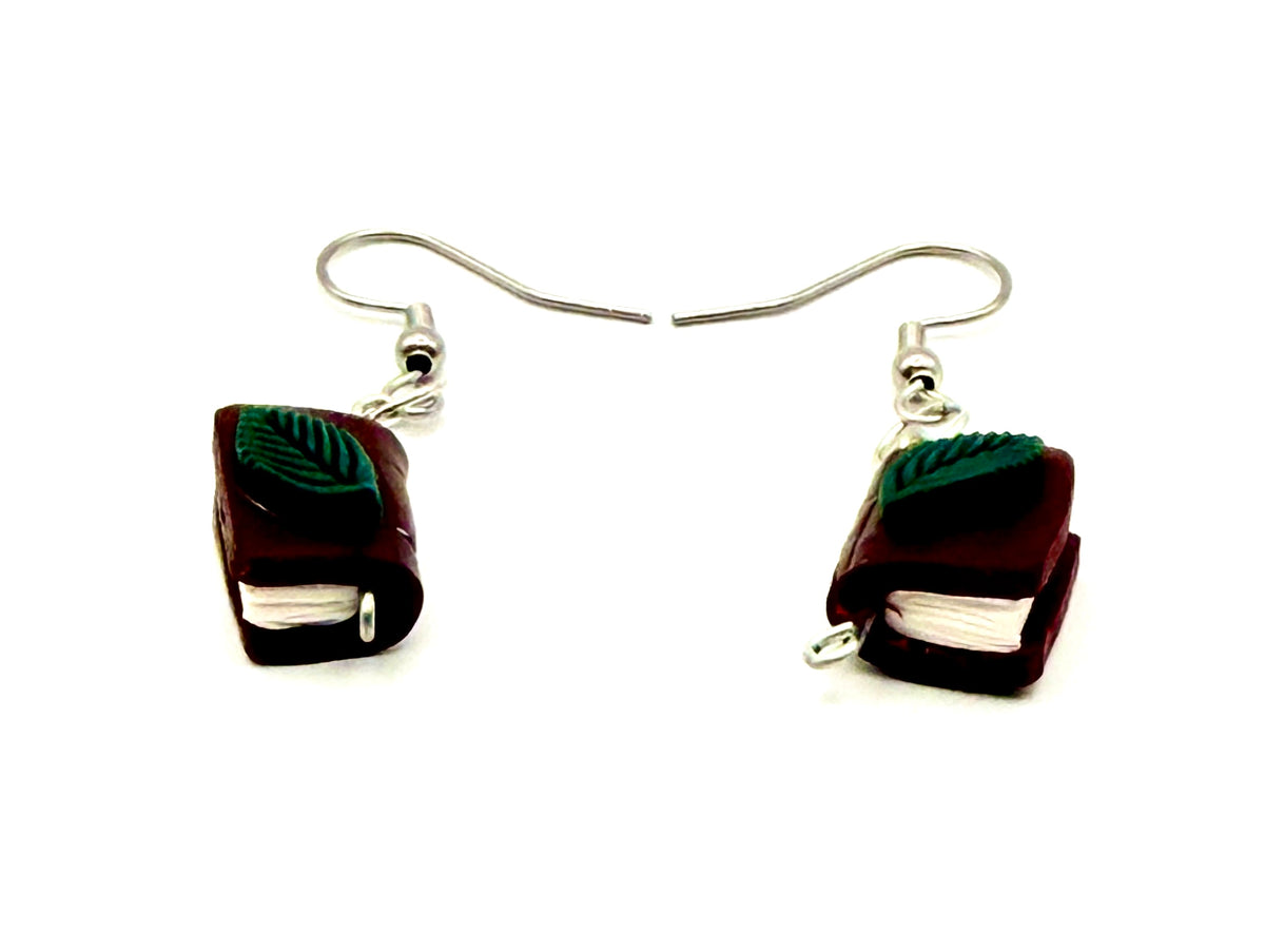 Maroon polymer clay book earrings with a green leaf on top. Suspended by a metal fishhook ear wire.