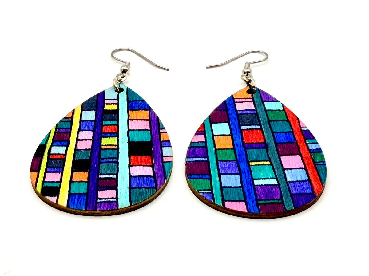 A pair of teardrop-shaped wooden drop earrings featuring a colorful, hand-painted geometric pattern of vertical stripes in various colors, suspended from silver fishhook wires on a plain white background.