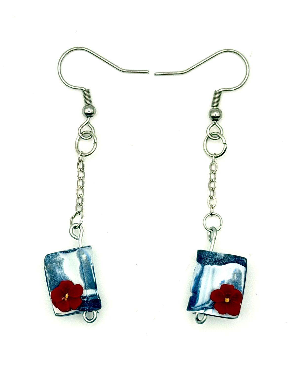 A pair of silver dangle earrings with rectangular blue and white marbled polymer clay book shaped pendants, each decorated with a small red poppy flower, shown on a plain white background.