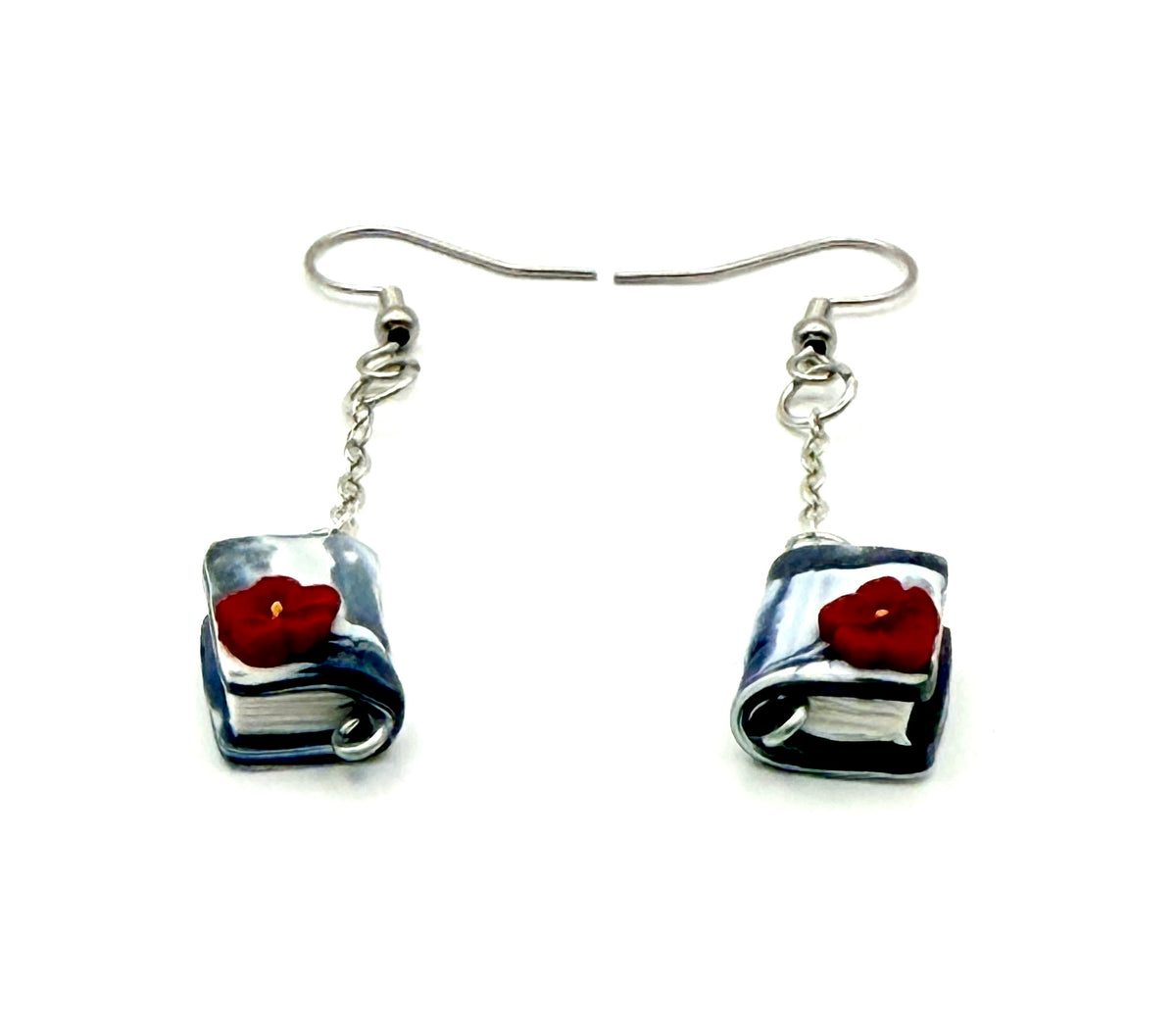 A pair of handmade earrings featuring miniature book charms with grey and white swirled covers and a small red poppy flower on each, suspended from silver fishhook wires against a plain white background.