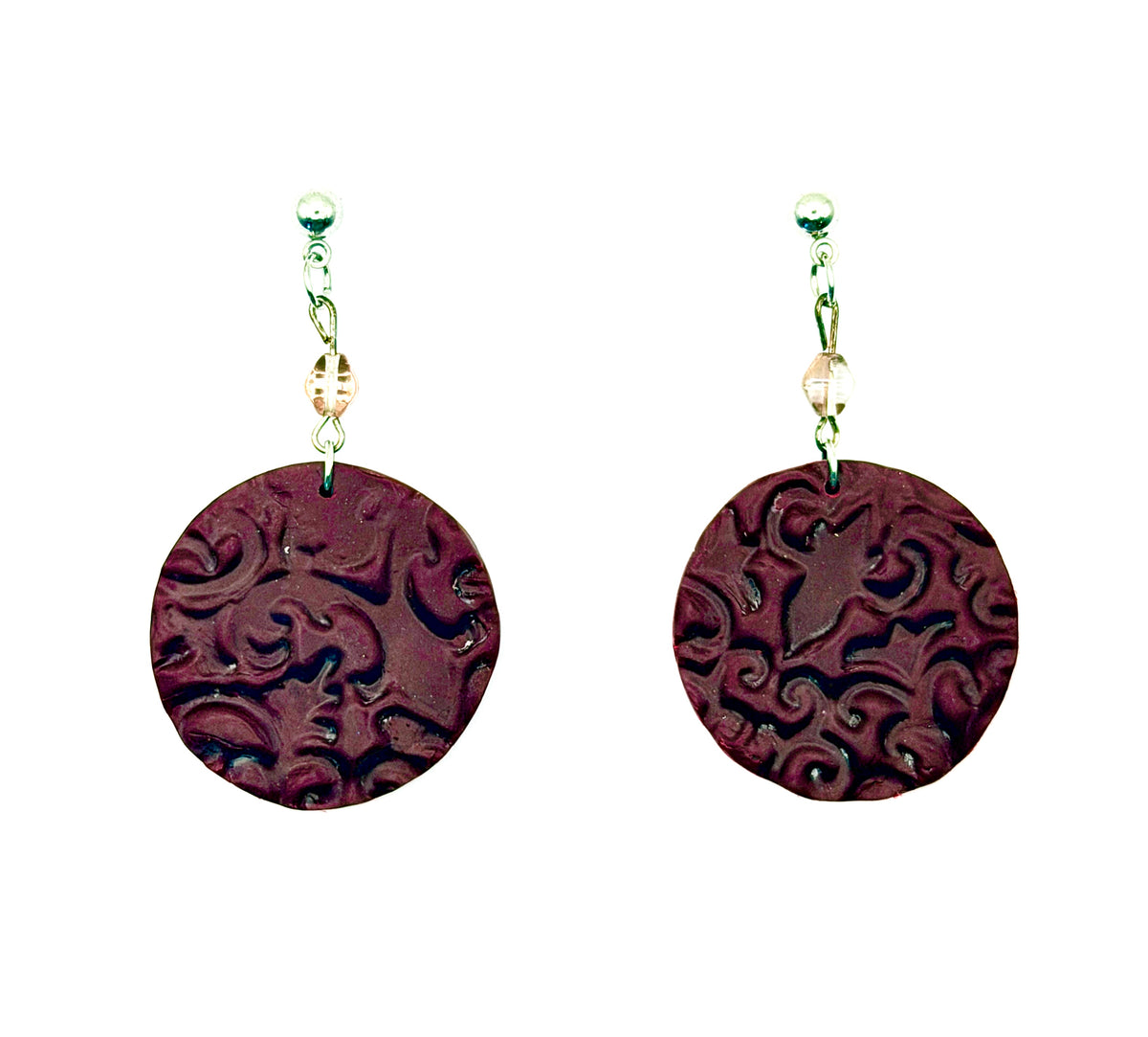 A pair of handmade drop earrings featuring round, dark reddish-brown polymer clay discs with intricate scrollwork, suspended from wire hooks with small clear beads on a white background.