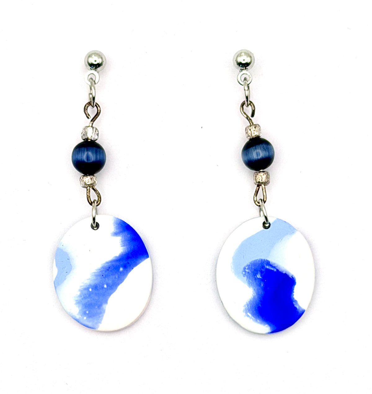 A pair of dangle earrings with silver-toned posts, dark blue beads, and oval white and blue marbled pendants on a white background.