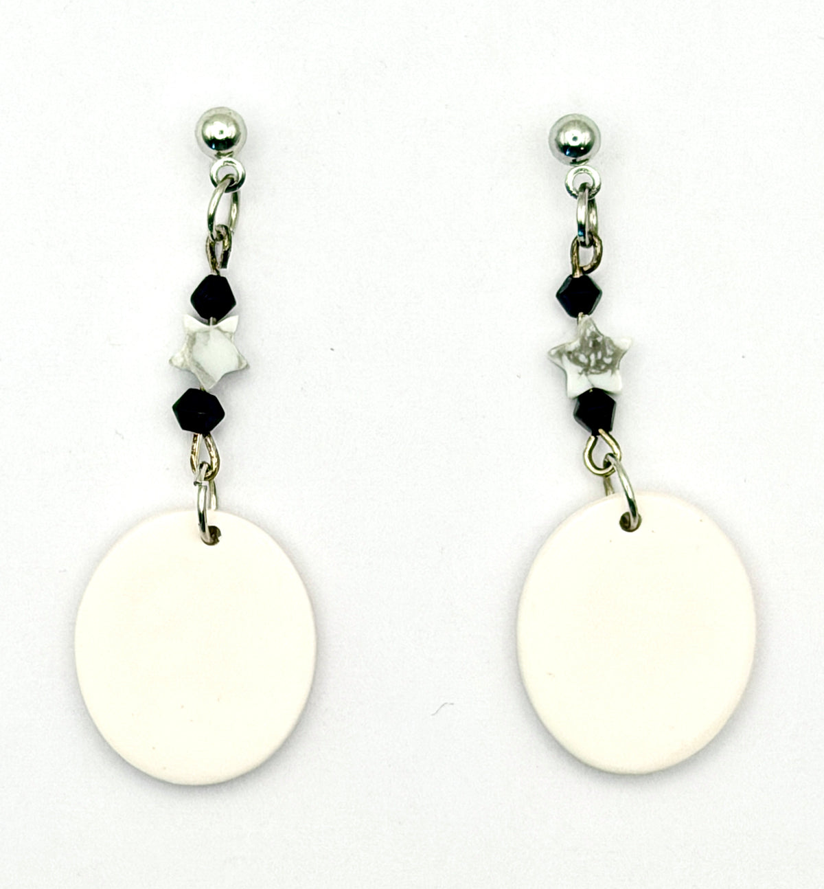 A pair of dangle earrings with large blank white oval charms, accented by small black and white beads and silver-toned metal posts on a white background.