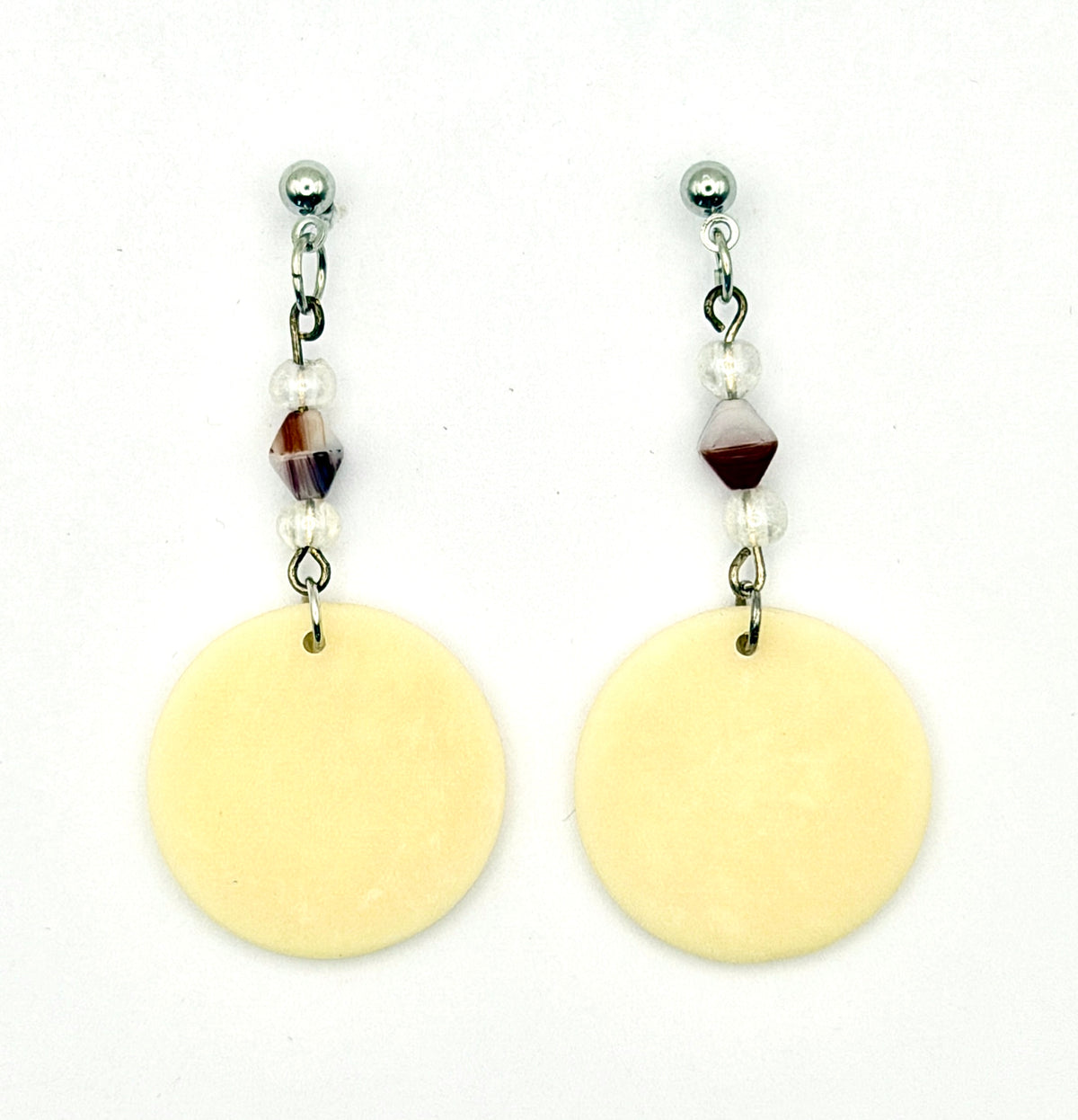 A pair of dangle earrings featuring large, flat, pale yellow circular disc charms hanging from silver-toned posts with small clear beads and a central maroon faceted bead, set against a plain white background.